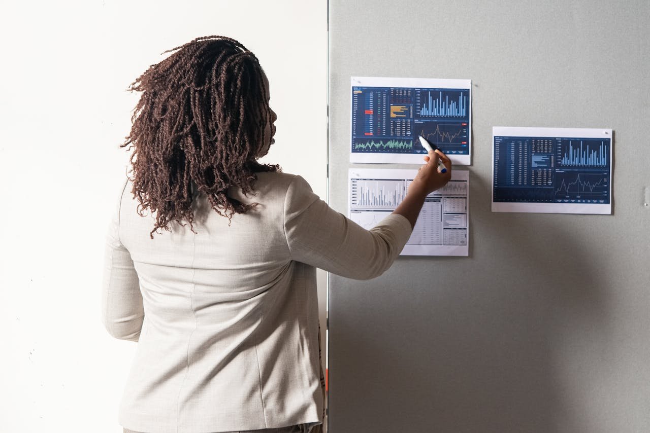 Photo of a Woman with Curly Hair Pointing at a Paper with a Graph